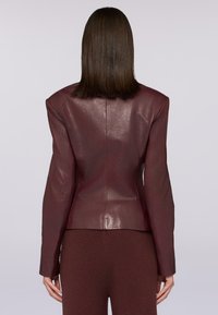 Giacca in pelle bordeaux con spalle strutturate, vestibilità su misura e superficie liscia. Progettata con una cucitura posteriore precisa e maniche lunghe.