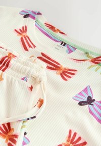 Kortærmet top med ribbet tekstur, der har farverige sløjfemønstre på en cremet baggrund og snørelukning nederst.