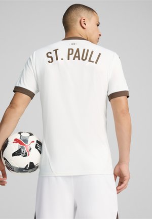 Valge jalgpallipusakas pruunide aktsentidega, mille seljal on rasvases kirjas "ST. PAULI". Rõivast täiendab must-valge jalgpall punase logoga.