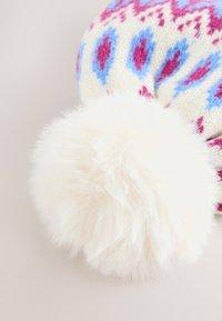 Berretto invernale lavorato a maglia color crema con motivi blu e rosa, che presenta un pompon in pelliccia ecologica bianca e soffice sulla sommità, dalla texture morbida.