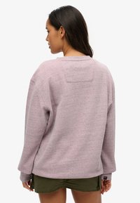 Różowy, oversize'owy sweter z fakturowanym wykończeniem, okrągłym dekoltem i opuszczonymi ramionami, w połączeniu z oliwkowymi szortami.