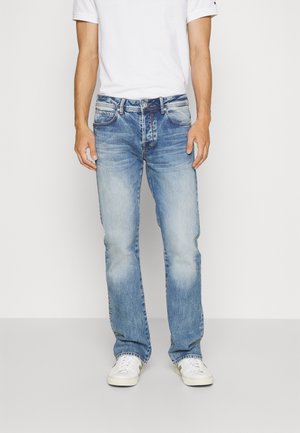 Ljusblå denimjeans med rak bendesign, fem fickor och subtila veck. Matchat med vita sneakers och en enkel vit t-shirt.