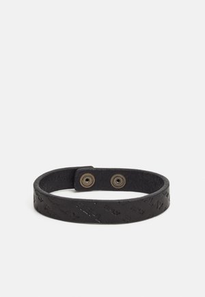 Schwarzes Lederarmband mit geprägtem Text und zwei Metall-Druckknöpfen zum Verschließen, auf weißem Hintergrund präsentiert.