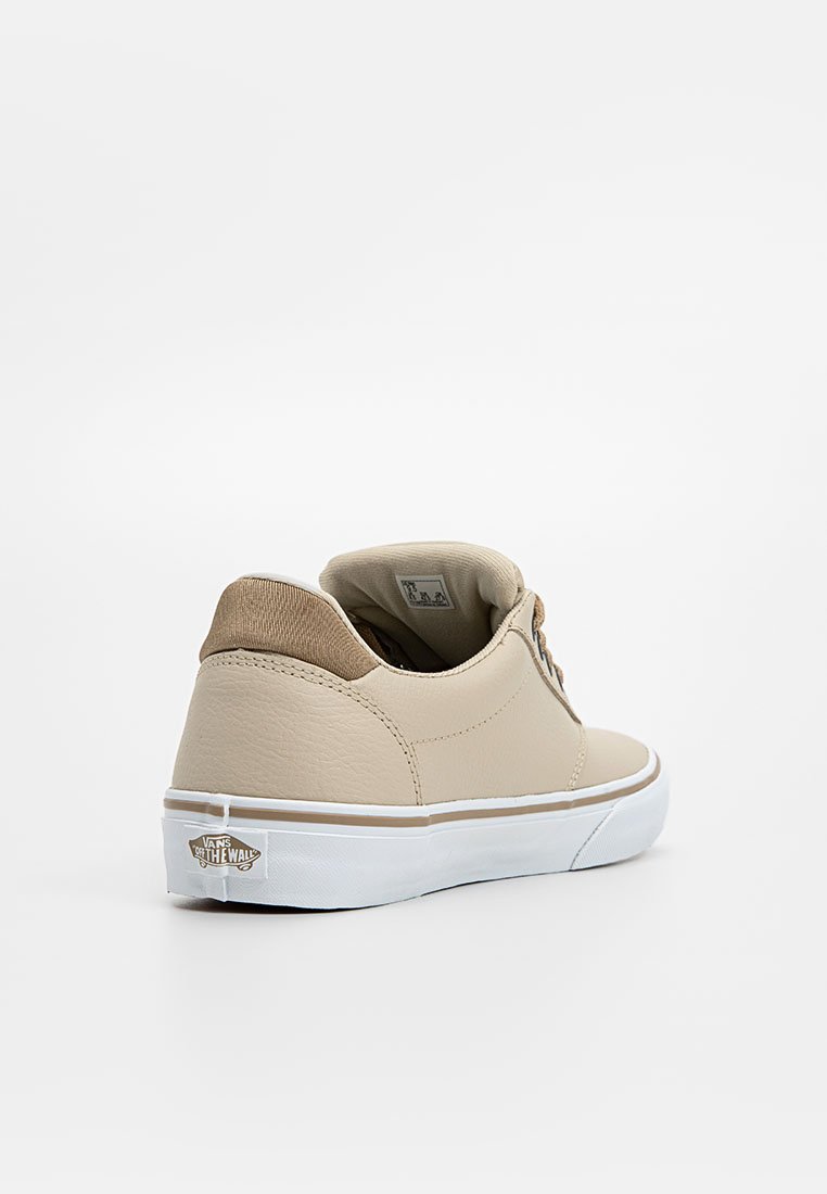 Zapatilla beige con cordones, con un upper de cuero texturizado, detalles en marrón, suela de goma blanca y una pestaña de talón con marca. Presenta un perfil bajo.