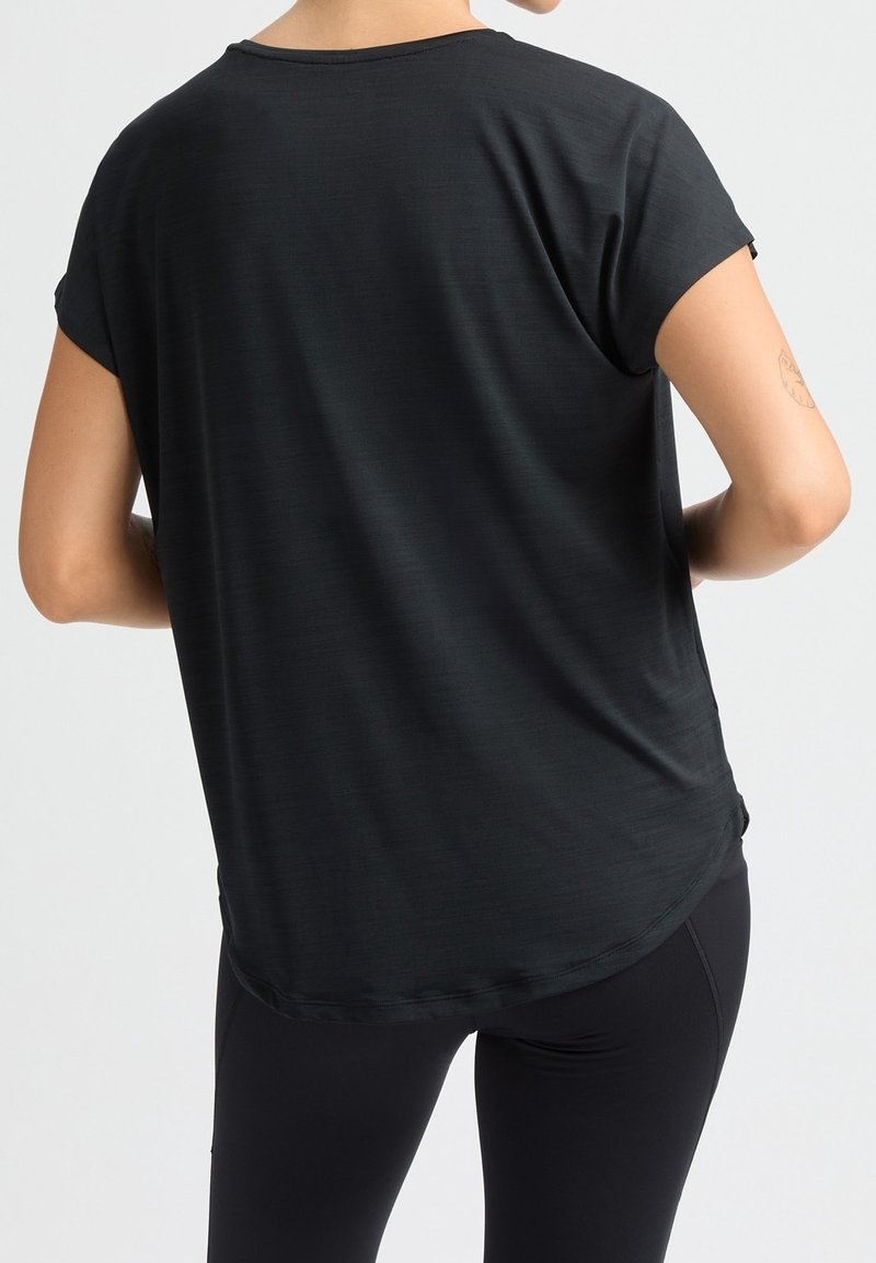 Personne portant un t-shirt noir ample à manches courtes et un legging noir, vue de dos avec les bras pliés aux coudes.