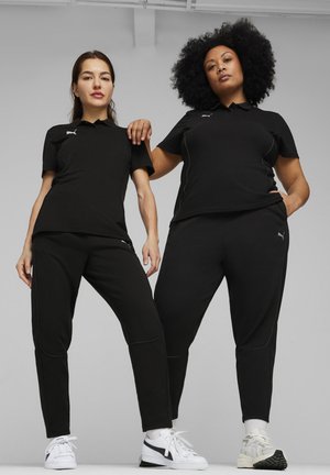 Schwarze Sportoutfits mit Kurzarm-Poloshirts und Hosen. Bemerkenswerte Details sind weiße Nähte und ein kleines Logo auf der linken Brust.