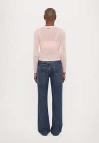 Lys rosa langermet topp med gjennomsiktig bakpanel, kombinert med vide mørkeblå jeans med lommer og rett snitt.