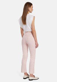 Jean rose clair à coupe slim, avec une taille mi-haute, des poches arrière, et un top blanc court. Le mannequin porte des chaussures beiges à enfiler.
