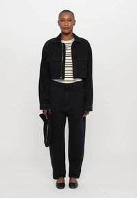 Chaqueta de mezclilla negra corta y jeans negros de cintura alta combinados con una blusa a rayas crema y negra y zapatos planos negros. Sosteniendo un bolso texturizado.