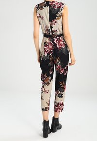 Blommig jumpsuit med en blandning av svart och beige tyg, korta ärmar, en figursydd midja med bälte och byxor i ankellängd.