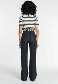 Zwarte wijde jeans met vijf zakken, hoge taille en een lichte vervaging. Gecombineerd met een gestreepte t-shirt met korte mouwen.