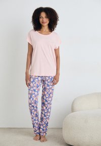 Šviesiai rožinė trumpomis Rankovėmis palaidinė su tekstu "Gerai išsimiegok"; derinama su mėlynomis gėlėmis raštuotomis kelnėmis, kuriose yra rožinių ir baltų gėlių. Minkšta medžiaga, laisvas kirpimas.