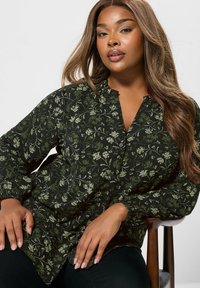 Schwarz-bluse mit floralem Muster und grünen Akzenten, Knopfleiste, gerafftem Ausschnitt und langen Ärmeln. Weicher Stoff mit femininer Musterung.