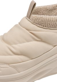 Μπεζ παπούτσι slip-on με επένδυση, υφασμένη σόλα και μαλακό ριμπ πλεκτό γιακά για άνεση και ζεστασιά.