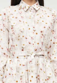 Φλοράλ φόρεμα από ελαφρύ, διάφανο ύφασμα με λευκή βάση, με παστέλ λουλουδένια σχέδια και ζώνη στη μέση. Γιακάς με κουμπιά.