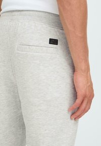Lichtgrijze sweatpants gemaakt van zachte stof, met een achterzak en een klein zwart label met witte tekst nabij de tailleband.