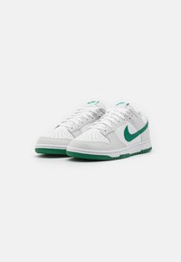 Tenis brancos da Nike com detalhes verdes. Apresentam couro liso, bico perfurado, colarinho acolchoado e sola de borracha com aderência texturizada.