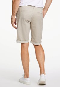 Pantaloni corti beige, lunghezza al ginocchio, con orlo arrotolato e due tasche posteriori, realizzati in tessuto testurizzato. Indossati con sneakers bianche.