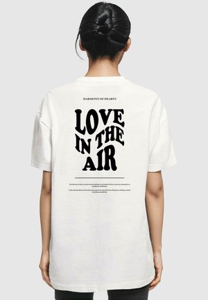 Weißes Baumwoll-T-Shirt mit fettem schwarzen Text auf dem Rücken, der "LIEBE IN DER LUFT" liest, sowie dekorativem Text darüber und darunter.