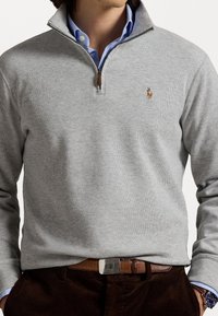 Pull-over gris à demi-fermeture éclair en mélange de coton, avec un petit logo brodé sur la poitrine, accompagné d'une chemise à col bleu clair.