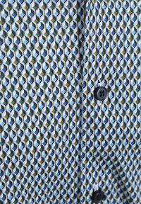 Katoenen overhemd met een geometrisch patroon in blauw, groen en zwart, met zwarte knopen langs de knopenlijst en een zachte textuur.