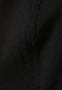 Schwarzer Stoff mit einer glatten Textur, der einen dezenten Glanz aufweist. Das Design enthält eine maßgeschneiderte Naht, die eine schlanke Silhouette betont.