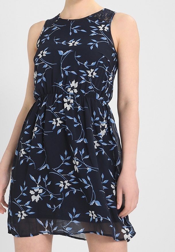 Robe sans manches bleu marine avec imprimé floral bleu et blanc, taille élastique et ourlet transparent portée par une personne sur un fond uni.