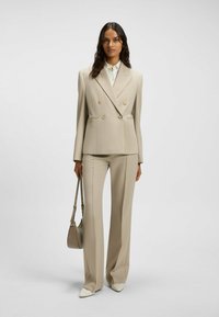 Beige double-breasted suit jacket with gold buttons, paired with matching flared trousers. Pointed cream heels and a light gray shoulder bag.