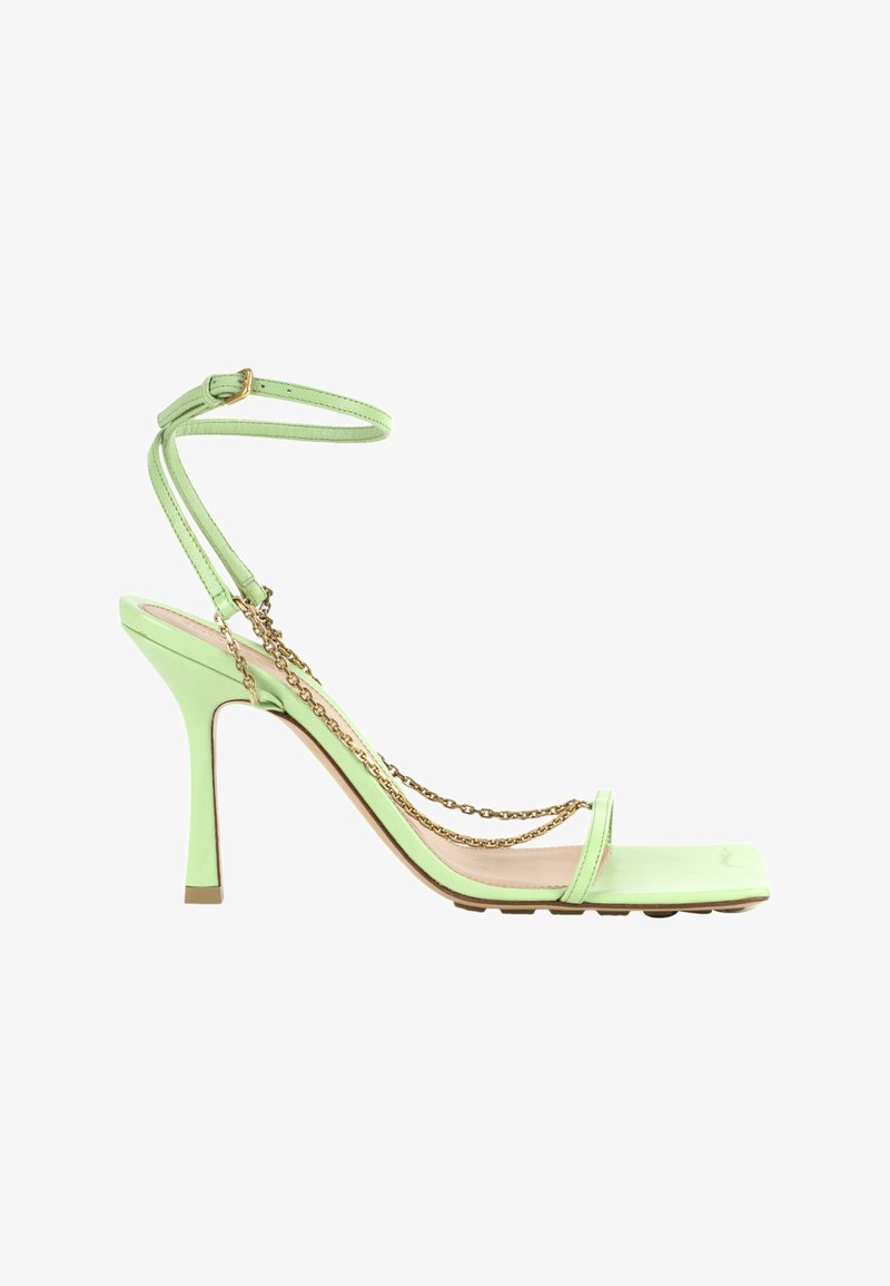 Sandale à talons hauts vert clair avec fines lanières, boucle à la cheville et délicates chaînes dorées drapées sur la semelle et les côtés.