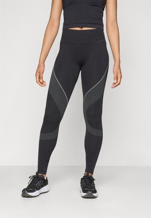 Leggings neri con vita alta, caratterizzati da un design testurizzato nelle tonalità più chiare e dettagli in rete lungo i lati. Abbinati a scarpe da ginnastica nere.
