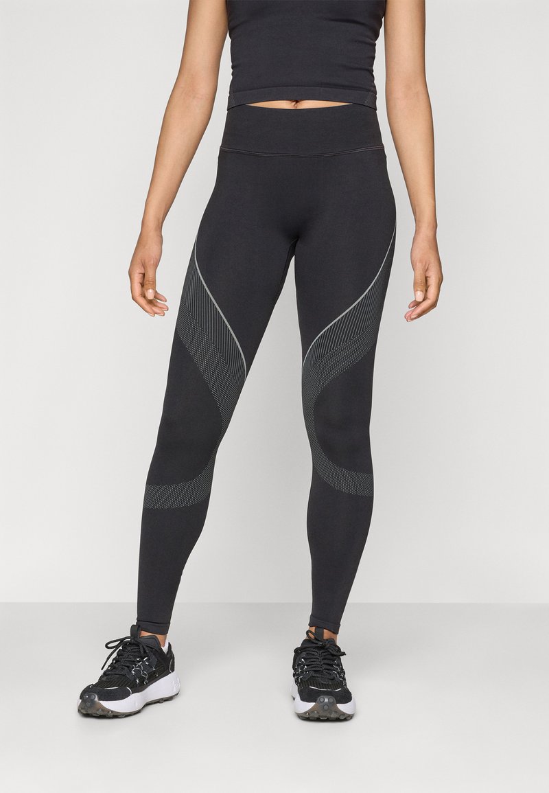 Fekete, magas derekú leggings, világosabb árnyalatokban texturált mintával és hálós részletekkel az oldalán. Fekete sportcipővel párosítva.