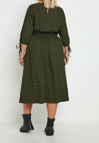 Kaki vihreä ruudullinen midi-mekko, jossa on rento leikkaus, joustava vyötärö ja nauhalla varustetut hihat. Mekossa on takana avainreikäaukko ja teksturoitu kangas.