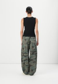 Haut noir sans manches associé à un pantalon ample camouflage en nuances de vert et de marron, avec des poches cargo et une silhouette décontractée.