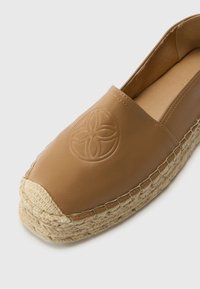 Tan nahkakengät espadrille, jossa on pyöristetty kärki, kyhätty juuttipohja ja kohokuvioitu kukkamuotoilu vampissa. Sileä pinta, minimaalinen ompelu.