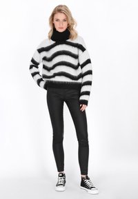 Zwart-wit gestreepte fuzzy trui met een hoge kraag, gecombineerd met zwarte skinny pants en zwarte sneakers. Zachte textuur en een ontspannen pasvorm.