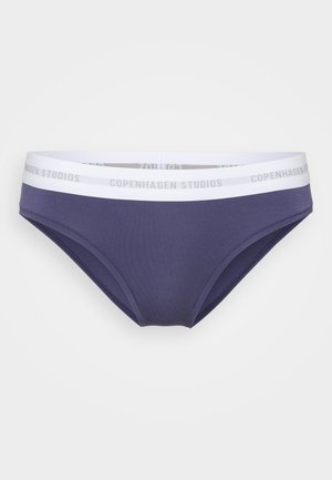 Mørkeblå trusser med en hvid elastisk talje, der viser teksten "Copenhagen Studios", præsenteret mod en ensfarvet lys baggrund.