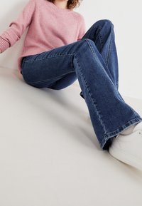 Light pink sweater with ribbed cuffs paired with dark blue flared jeans and white sneakers, showcasing a casual outfit.