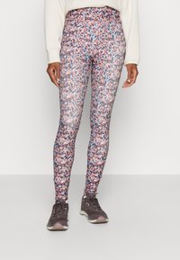 Legginsy z wysokim stanem w intensywny kwiatowy wzór z odcieniami różu, niebieskiego i białego; gładki, elastyczny materiał; zestawione z szarymi sneakersami.