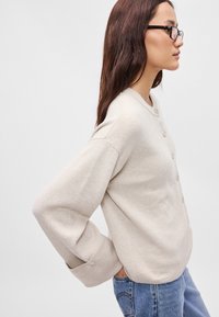 Μπεζ πουκάμισο με κουμπιά, με ριγωτή υφή, στρογγυλή λαιμόκοψη και χαμηλωμένους ώμους, σε συνδυασμό με μπλε τζιν.