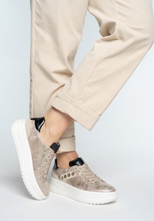 Legs in beige corduroy pants with cuffs rolled up, wearing taupe suede sneakers with white thick soles and black heel accents.