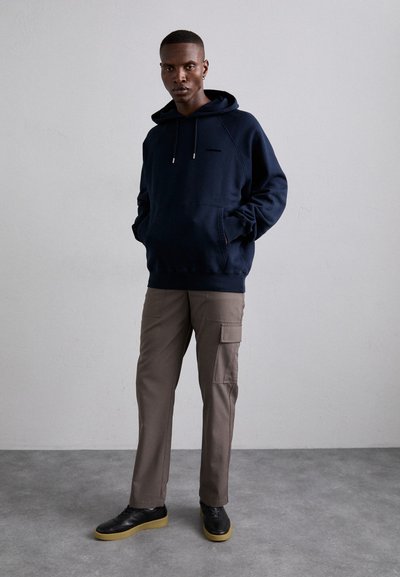 Felpa navy con cappuccio e cordini, abbinata a pantaloni cargo beige con tasche laterali e scarpe nere con suola in gomma.