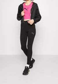 Giacca crop nera, top aderente rosa e leggings neri con logo. Scarpe da ginnastica nere con calzini bianchi. Design e texture semplici.
