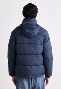 Chaqueta acolchada azul marino con capucha, con costuras horizontales y puños elásticos, diseñada para brindar calidez y comodidad.