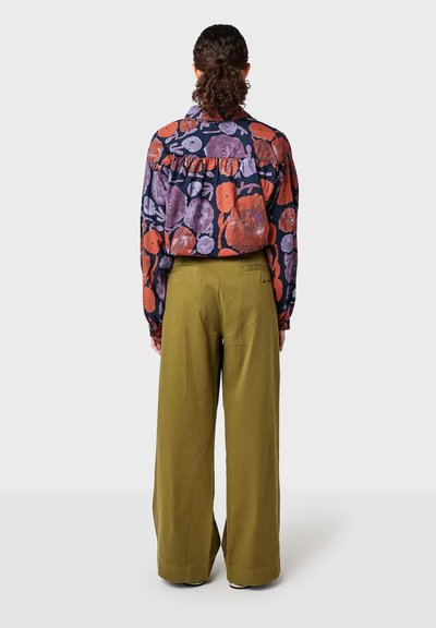 Langarmshirt met een multikleurig bloemenpatroon in paars en rood, gedragen met hoge taille olijfgroene brede broek.