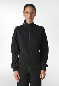 Giacca nera con zip, colletto alto, maniche arricciate e polsini a costine. Realizzata in un materiale morbido, progettata per un look aderente.