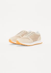 Baskets beiges en matériau mesh et suède, dotées d'une semelle en caoutchouc blanc et d'une semelle d'adhérence orange. Six œillets avec des lacets assortis.