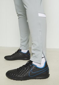 Graue Sporthosen mit seitlichen Schlitzen, kombiniert mit schwarzen, strukturierten Sneakers mit blauen Akzenten und weißen Crew-Socken.