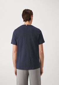Camiseta de algodón azul marino con cuello redondo, mangas cortas y una pequeña etiqueta de color en el escote. Textura suave, corte relajado.