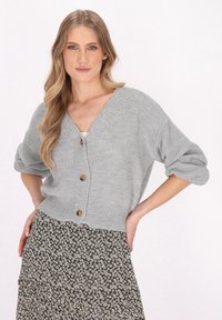 Cardigan gri, tricotat, cu decolteu în V, trei butoane mari și mâneci largi. Asortat cu o fustă cu model floral.