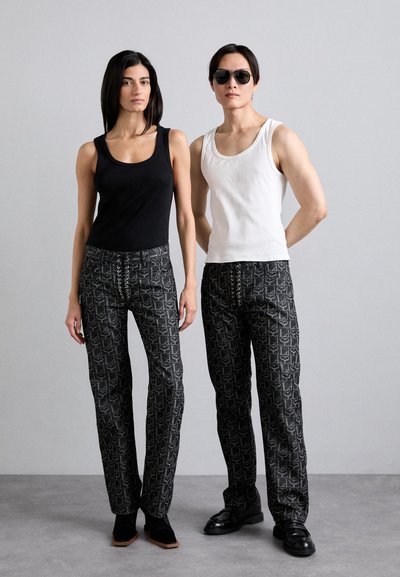Des débardeurs noir et blanc associés à des pantalons noirs à motifs carrés avec des détails de lacets. Le mannequin à gauche porte un débardeur noir, tandis que le mannequin à droite porte un débardeur blanc.